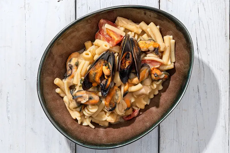 Piatto di pasta con fagioli e cozze, condita con pomodorini e una cremosa salsa.