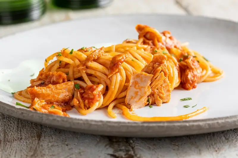 Spaghetti al tonno conditi con un sugo saporito e ricchi pezzi di tonno, guarniti con prezzemolo fresco.