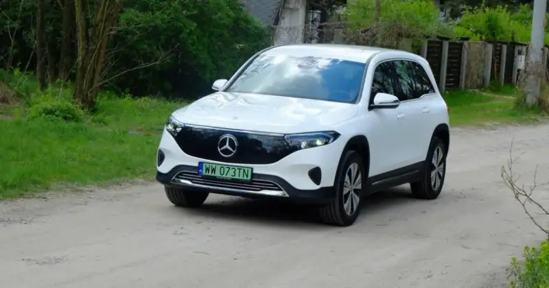 Biały Mercedes EQB na drodze gruntowej, otoczony zielenią.