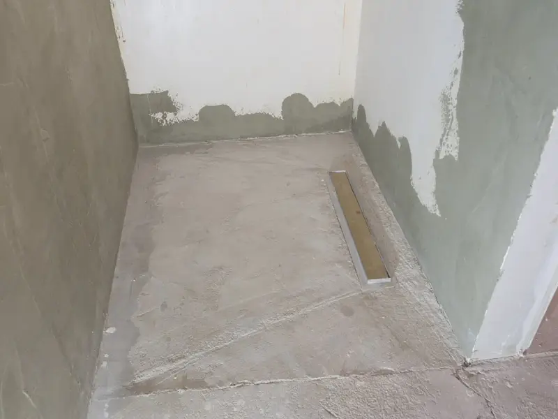Niedawno położony szlam mineralny w łazience, z widocznym odpływem liniowym. Ściany w trakcie tynkowania.