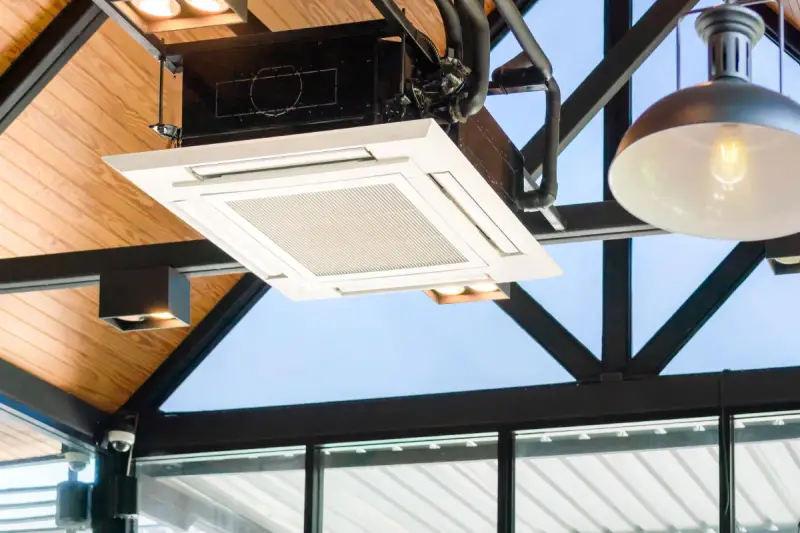 Unidad de cassette de un sistema VRV integrada en un techo de madera y metal, con luces y tuberías visibles.