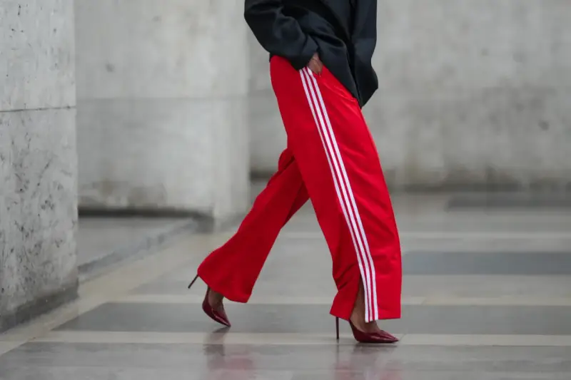 Czerwone spodnie dresowe z białymi lampasami i eleganckie szpilki. Odważne połączenie, które odpowiada na pytanie: jakie buty do dresów?