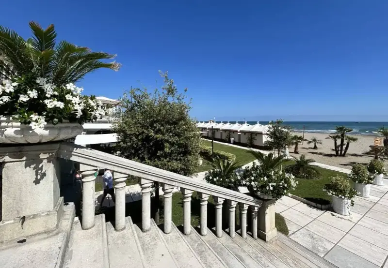 Scalinata in pietra con vasi fioriti, vista su una spiaggia ordinata con cabine bianche, tipica di una città di mare veneto.