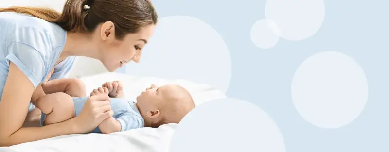 Uśmiechnięta mama pochyla się nad dzieckiem, które świadomie mówi "mama".