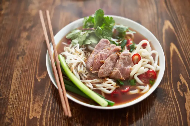 Un bol de soupe nouille de riz avec du bœuf, des germes de soja, des oignons verts et du piment rouge, prêt à être dégusté avec des baguettes.