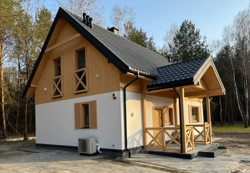 Nowy dom w lesie, drewniane elementy i biały tynk. Prowadzenie budowy domu zakończone sukcesem, gotowy do zamieszkania.