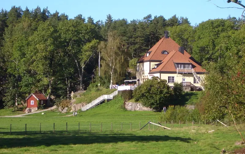 Gula huset vid grinda Stockholm, med röda stugor och grönskande träd.