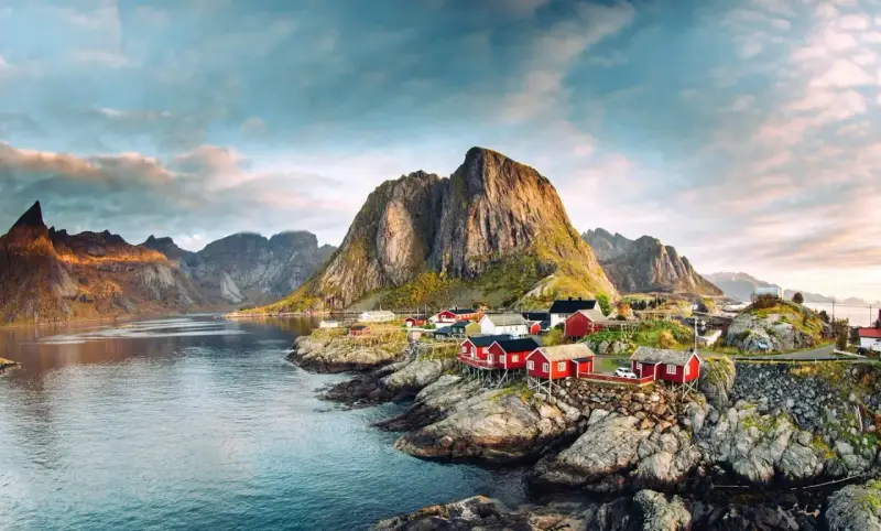 Röda fiskestugor vid en vik, med dramatiska berg i bakgrunden. En idyllisk vy som visar var ligger Lofoten.