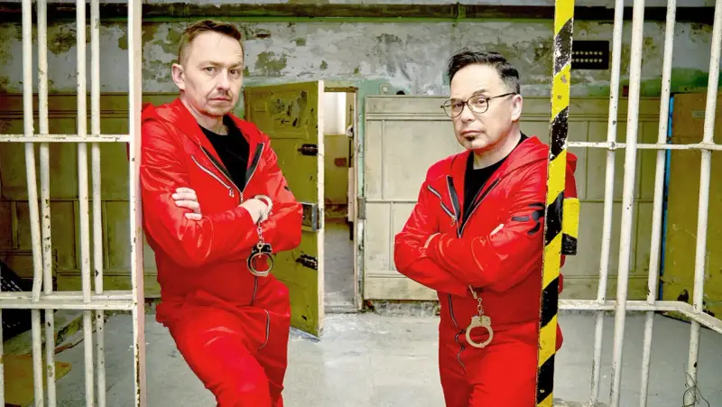 Dwóch mężczyzn w czerwonych kombinezonach i kajdankach, gotowych do ucieczki. Czy uda im się unlock po polsku?