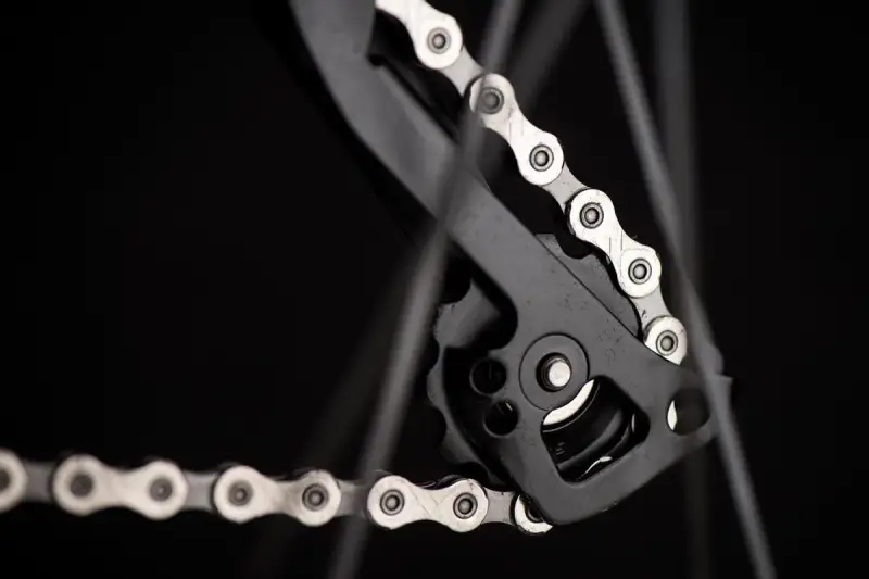 Zbliżenie na mechanizm przerzutki z łańcuchem rowerowym. Widać ogniwa i rolki, kluczowe dla łańcuch rowerowy wymiary.