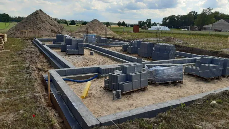 Budowa fundamentów z bloczków betonowych. Zastanawiasz się, ile kosztuje wylanie fundamentu? Na placu budowy widać materiały i postęp prac.