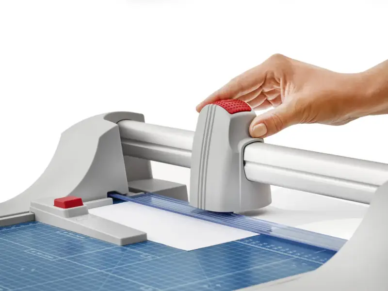 Mano operando una guillotina o cizalla para cortar papel con precisión.