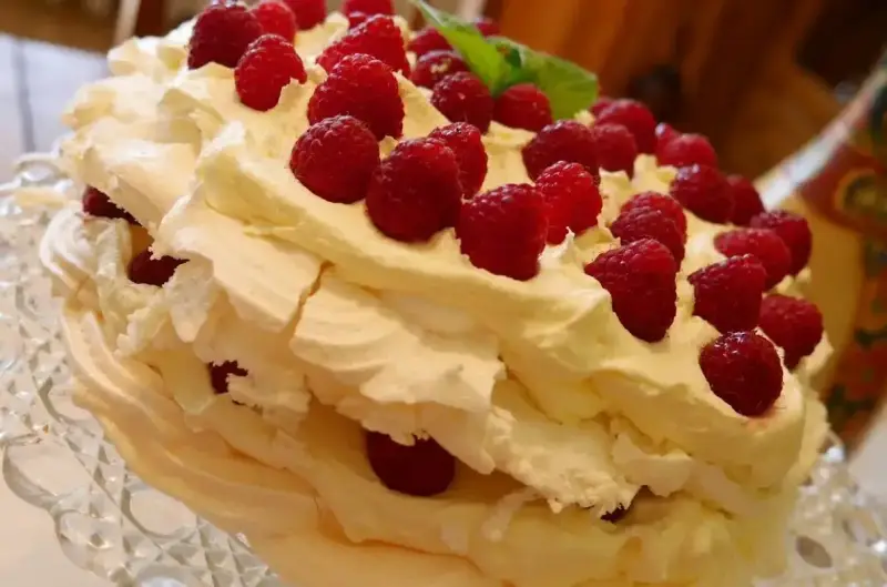 Puszysty, wielowarstwowy tort bezowy z bitą śmietaną i malinami. Wygląda jak najpyszniejszy tort bezowy, jaki można sobie wyobrazić!