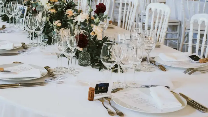 Un élégant dressage d'une table à la française, prêt pour un festin. Verrerie étincelante, fleurs fraîches et menus attendent les convives.