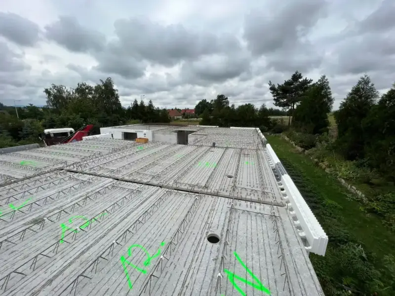 Gotowy do wylania strop, zbrojenie czeka na beton. W tle drzewa i pochmurne niebo.