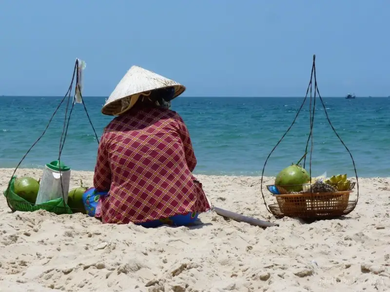 Sprzedawczyni kokosów na plaży w Mui Ne, Wietnam. W tle błękitne morze i niebo.