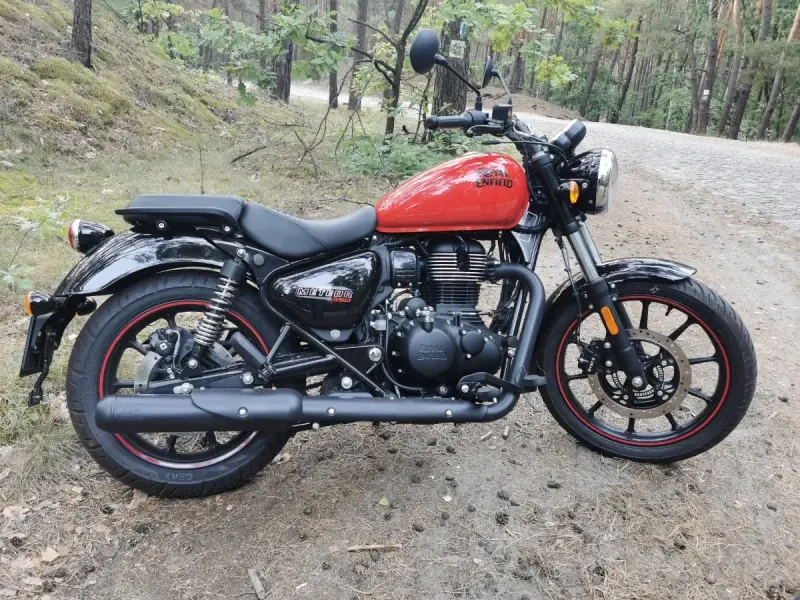 Czerwony Royal Enfield Meteor 350 na leśnej drodze. Klasyczny wygląd i nowoczesna technologia w jednym.