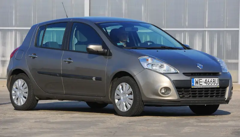 Szary Renault Clio 3 z kierowcą za kierownicą, zaparkowany na zewnątrz.