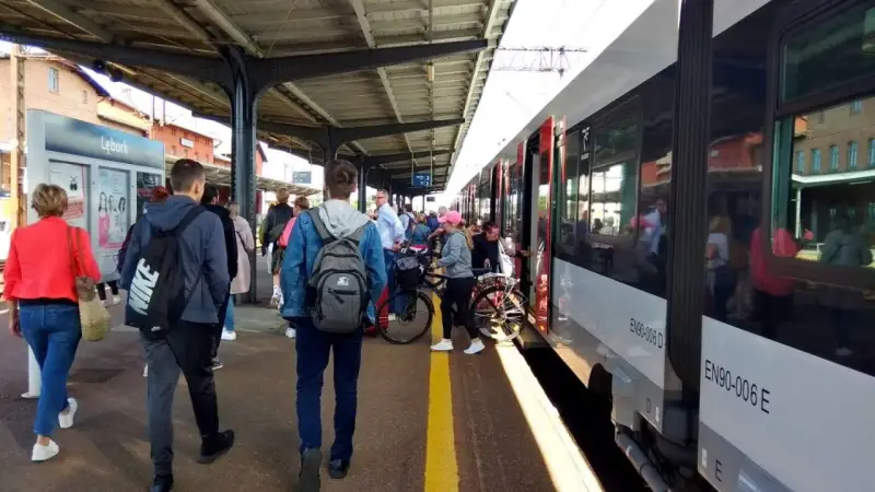 Ludzie czekają na pociąg na stacji w Lęborku. W tle widać budynek dworca i peron.