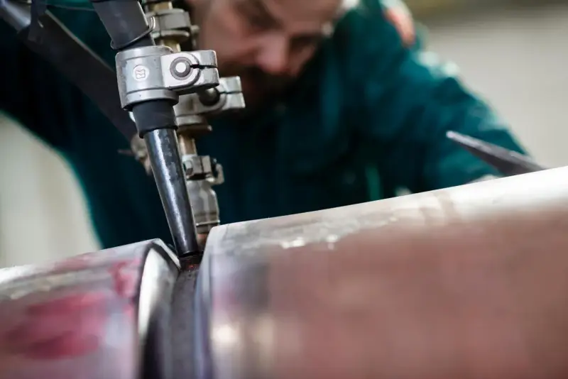 Saldatore esperto esegue saldatura ad arco sommerso su un tubo metallico, creando un giunto robusto.