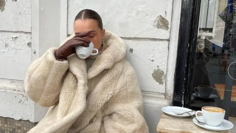 Vanilla girl w kremowym futrze pije kawę, otulona ciepłem i spokojem.
