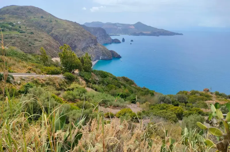 Panoramica mozzafiato per capire come visitare le Isole Eolie: costa verdeggiante, mare blu intenso e isole vulcaniche all'orizzonte.