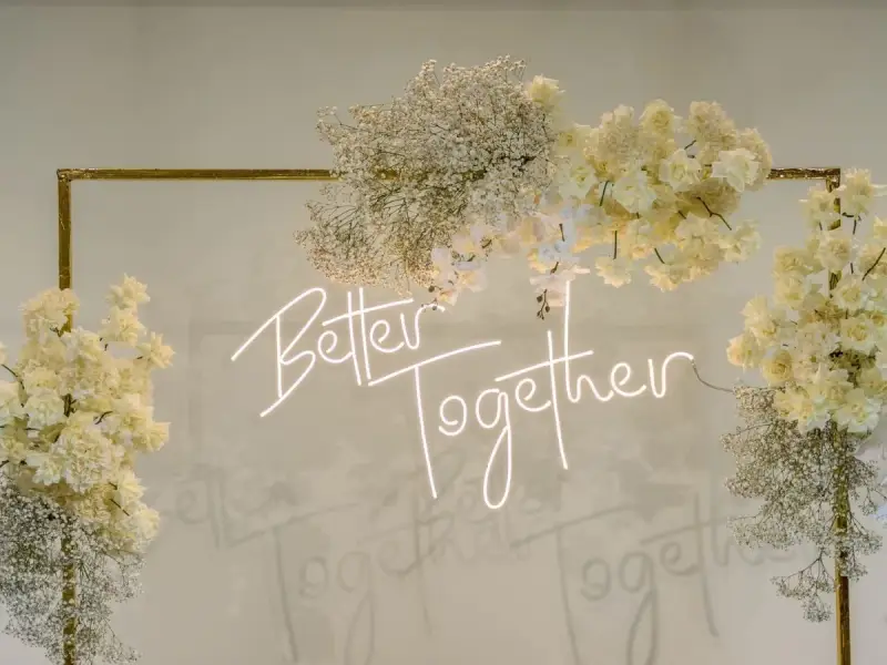 Elegancka ściana z kwiatów w kremowych odcieniach, ozdobiona neonowym napisem "Better Together".