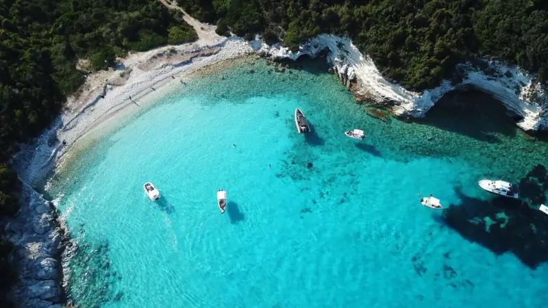 Idealne wakacje na Paxos: turkusowa woda, białe skały i łodzie unoszące się na falach.