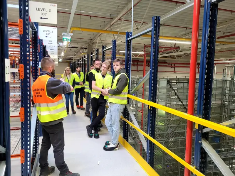 Grupa osób w kamizelkach odblaskowych zwiedza magazyn CEVA Logistics. To potencjalna ceva logistics praca.