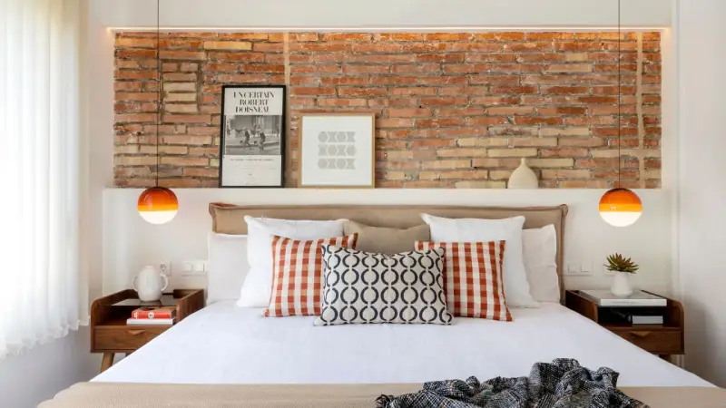 Ideas para decorar la pared de la cabecera de la cama: ladrillo visto, cuadros y lámparas naranjas.