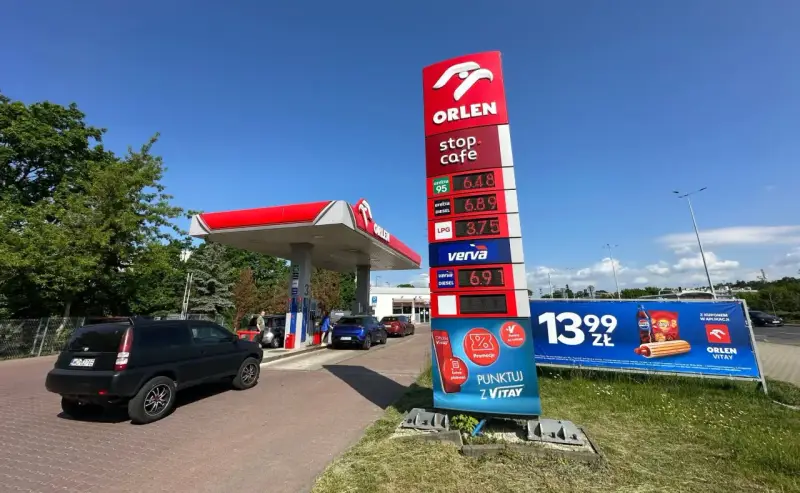 Stacja paliw Orlen z cennikiem paliw: benzyna 95 za 6.48 zł, diesel za 6.89 zł, LPG za 3.75 zł. Obok reklama hot doga i napoju.