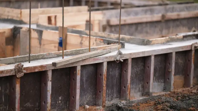 Drewniany szalunek czeka na beton. Widać zbrojenie i świeży beton.