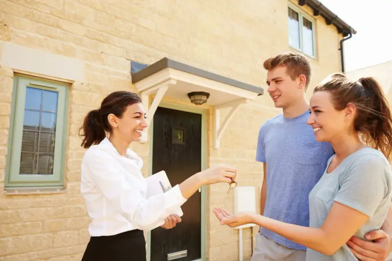 Une agent immobilier remet les clés d'une maison à un jeune couple. Ils sont heureux d'acquérir leur nouveau logement, peut-être grâce au droit de préemption locataire.