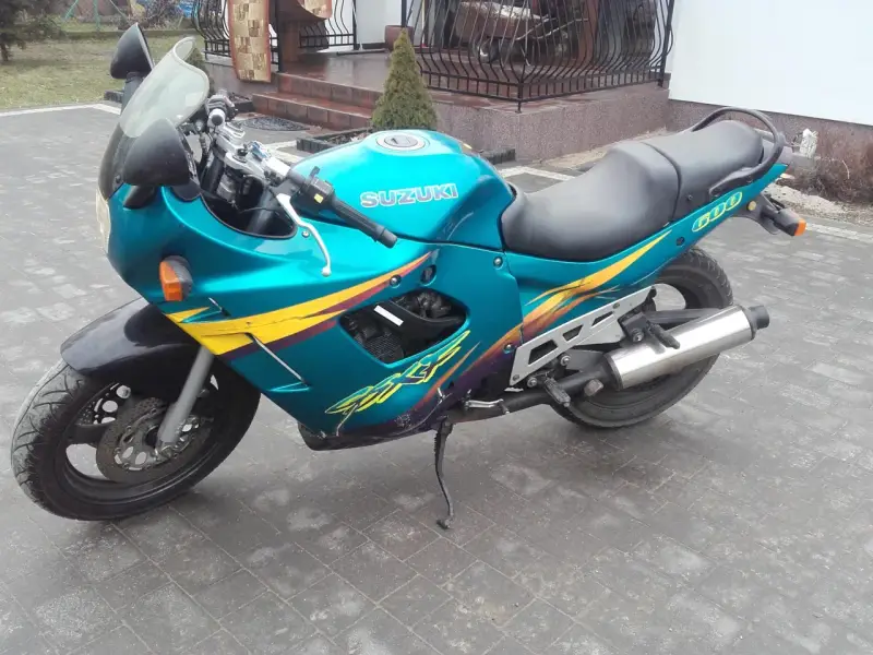 Turkusowy Suzuki GSXF 600 z żółto-fioletowymi grafikami, zaparkowany na kostce brukowej przed domem.