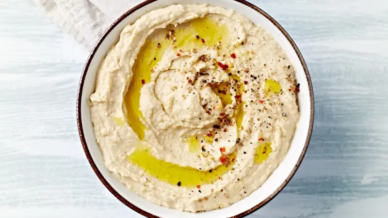 Kremowy, gładki hummus polany oliwą i posypany przyprawami. Idealny do maczania pieczywa.
