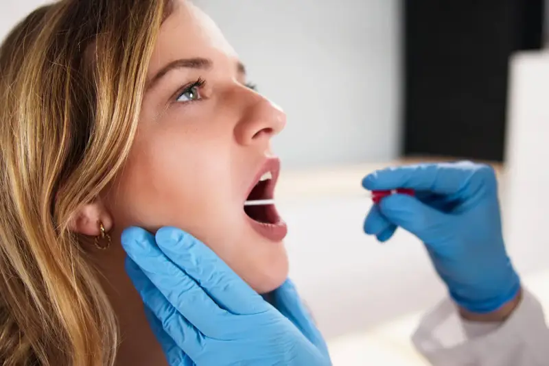 Młoda kobieta z otwartymi ustami, której gardło jest badane patyczkiem do testu strep.