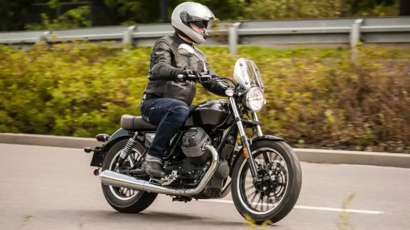 Motocyklista w kasku i skórzanej kurtce jedzie na stylowym motocyklu Moto Guzzi V9.