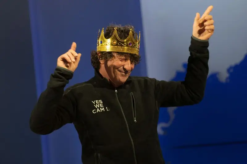 Jean Le Cam, le roi des mers, porte une couronne dorée et une veste noire avec l'inscription "YES WE CAM L".