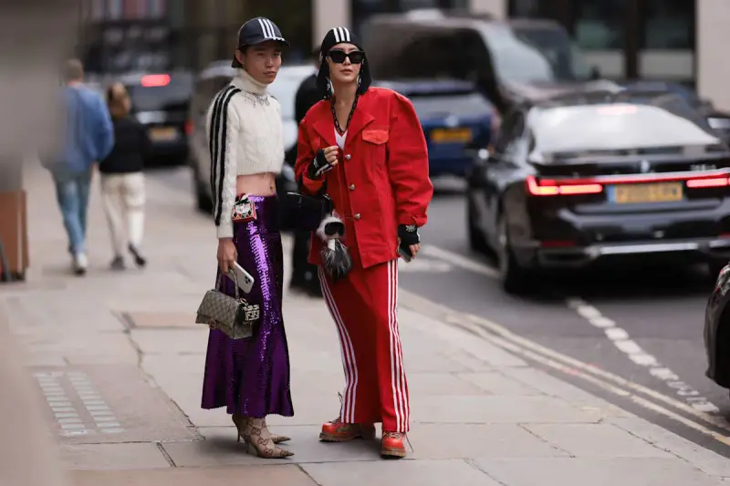 Zwei Personen präsentieren ihren **new money style** auf der Straße: glitzernder lila Rock, rote Jacke und sportliche Elemente.