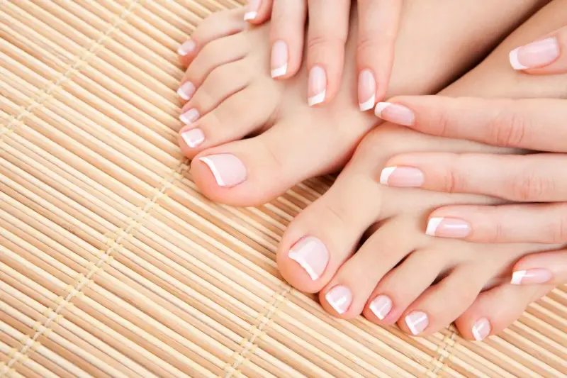 Dłonie i stopy z perfekcyjnym pedicure french na bambusowym tle.