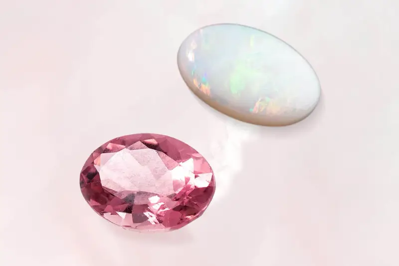 Pink tourmaline and opal, the two birthstones for October, shimmer on a pale background.