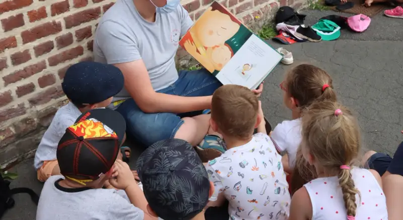 Un animateur lit un livre illustré à des enfants assis en cercle. L'image évoque un moment de partage et d'apprentissage, comme un diplôme animation.