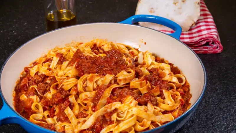 Herzhafte Tagliatelle mit einer reichhaltigen alla bolognese Sauce in einer blauen Pfanne, bereit zum Servieren.