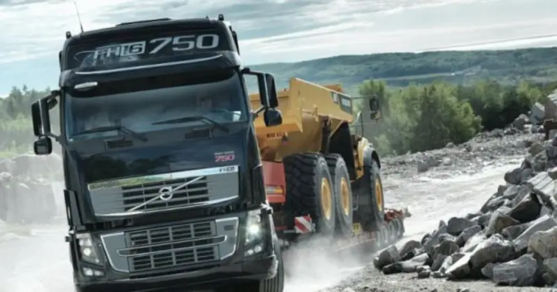 Ciężarówka Volvo FH16 750 z naczepą przewozi żółty wozidło przegubowe przez kamieniołom.