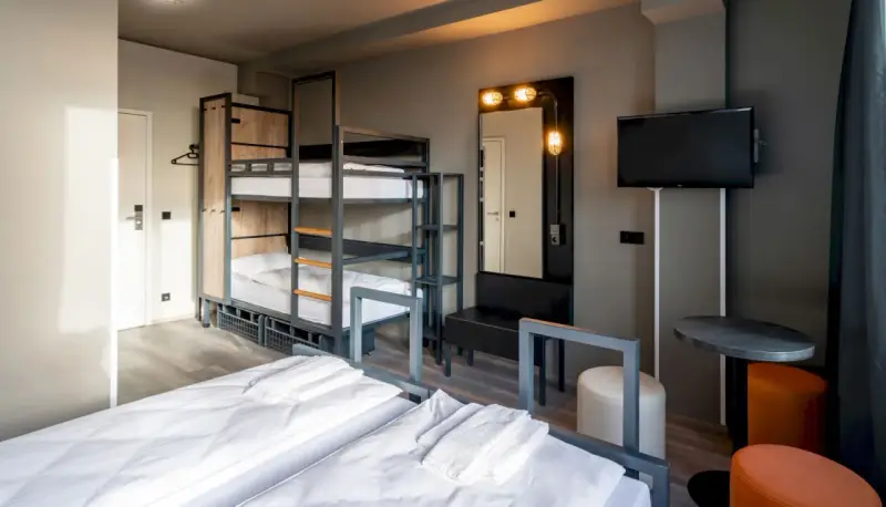 Pokój wieloosobowy w hotelu a&o Warszawa z łóżkami piętrowymi, dwoma łóżkami pojedynczymi i telewizorem.