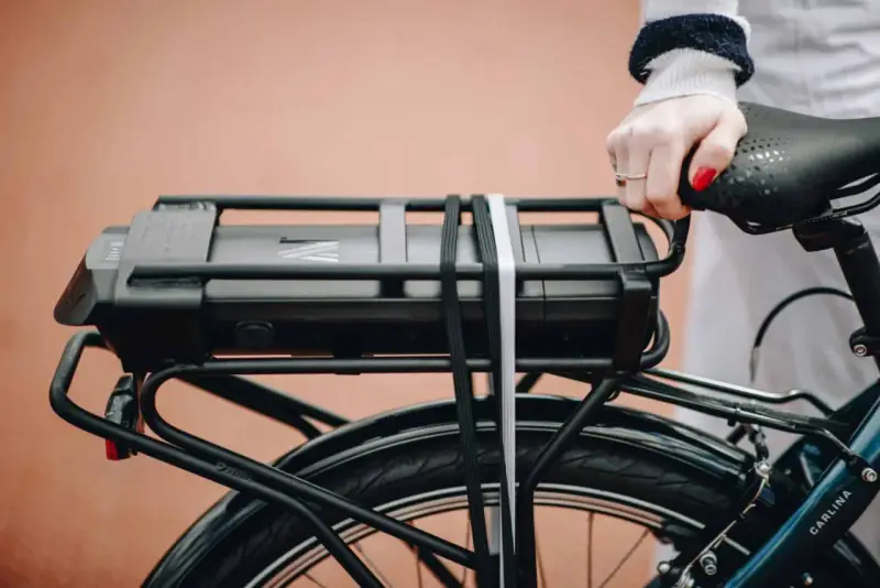 Main d'une femme tenant la selle d'un vélo électrique, avec la batterie visible sur le porte-bagages. Idéal pour tester la batterie du vélo.
