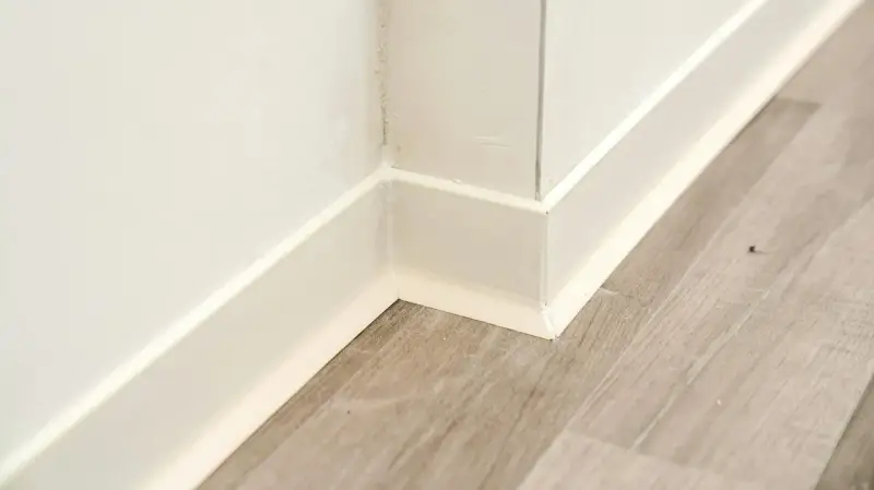Angolo di una stanza con parquet grigio e battiscopa bianco appena installato.