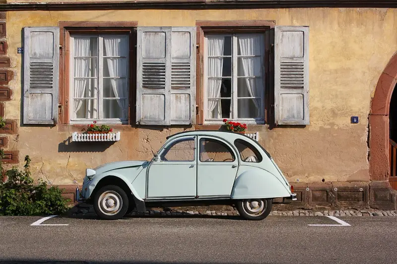 Jasnoniebieski, zabytkowy Citroen 2CV, jeden z klasycznych modele stare, parkuje przed kamiennym domem z drewnianymi okiennicami.