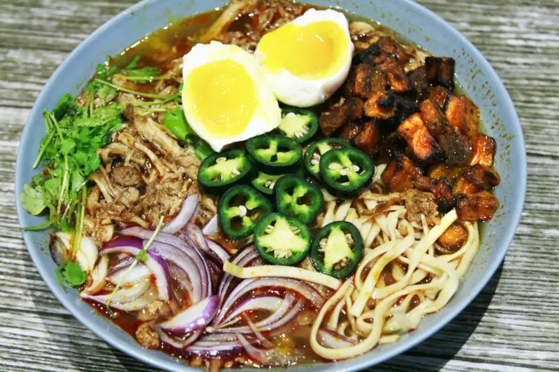 A miseczce ramen z wieprzowiną, jajkiem na pół, papryczkami jalapeño, cebulą i kolendrą.