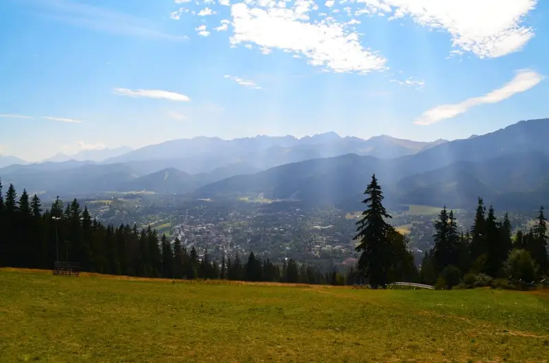 Widok na Zakopane z Gubałówki. Słońce przebija się przez chmury, oświetlając miasto i góry. Zastanawiasz się, ile się idzie na Gubałówkę?
